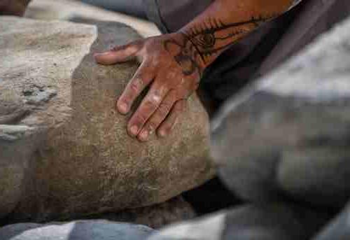 Artist Jason Quigno lays his hand on a stone