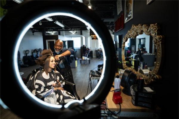 Salon owner Jerry Wright works on a client's hair, they are projected in a mirror