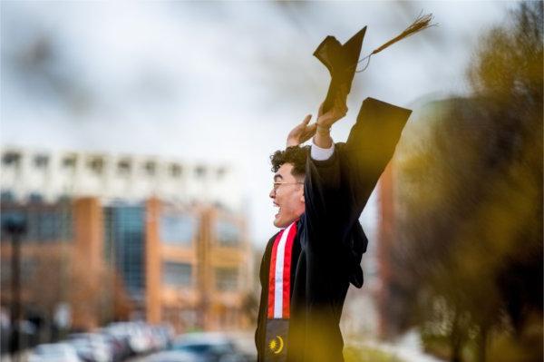一名研究生戴着毕业帽，身穿黑色毕业服，兴奋地举起双臂. 