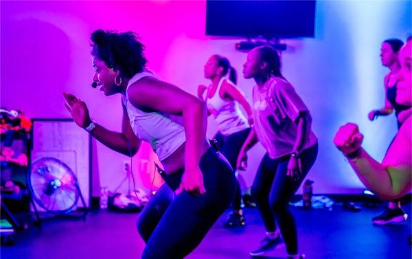 一名健身教练在一间有蓝紫色灯光的彩色房间里带领学生锻炼. 