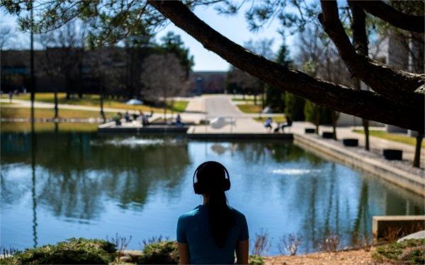一个戴着耳机的大学生在池塘边的剪影.  