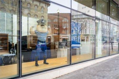 一所大学的吉祥物站在一家新开的店面里伸展肌肉，橱窗里映出一座城市.