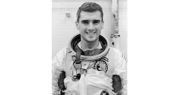 A person wearing an astronaut uniform smiles in a black and white photo.