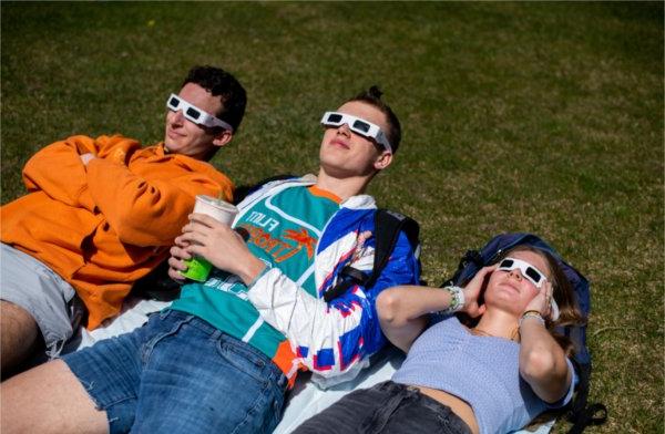 三个人躺在地上，戴着特殊的日食眼镜. 他们仰望天空.