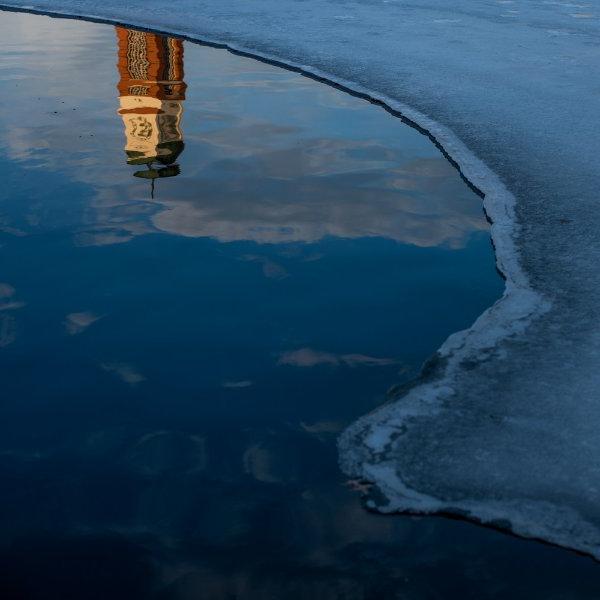 Carillon塔倒映在Zumberge池塘的水里，左边有一条冰的曲线.