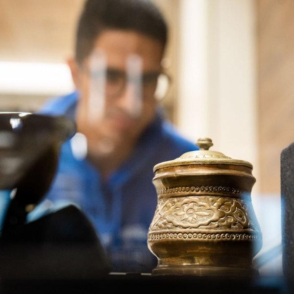 student with glasses looks through a case at a piece of artwork, an Iranian sugar bowl