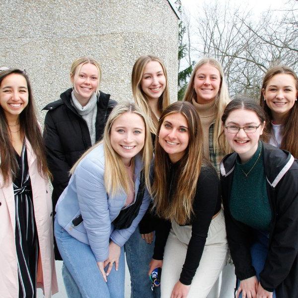 eight students are pictured standing in two rows in front of a building on the Allendale Campus