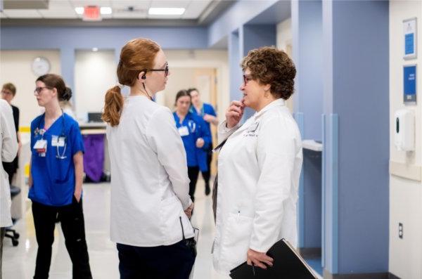KCON的员工Sally Stockdale说, 左, 和布里安娜·哈钦森在模拟中心医院套房的走廊里谈话. 12名教职员工和3名Corewell健康中心的护士参加了模拟实验.