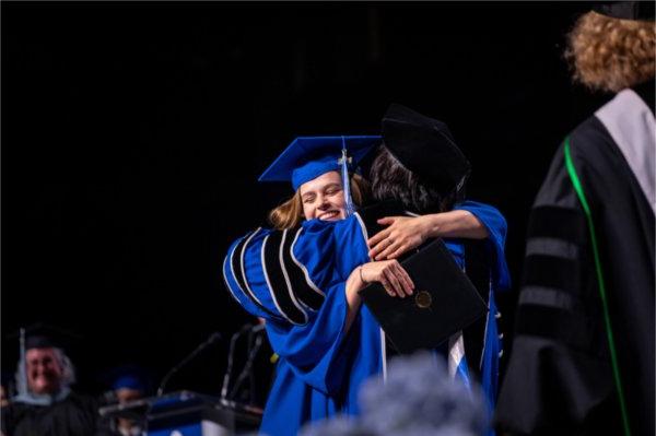  一名毕业生在接受毕业证书时拥抱了大学校长.